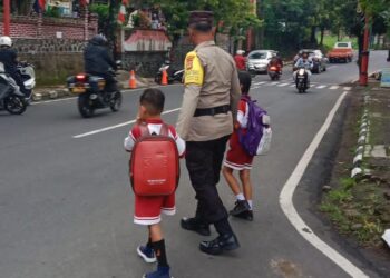Potret Bhabinkamtibmas Kelurahan Gianyar Rutin Menolong Anak Sekolah Seberangi Jalan